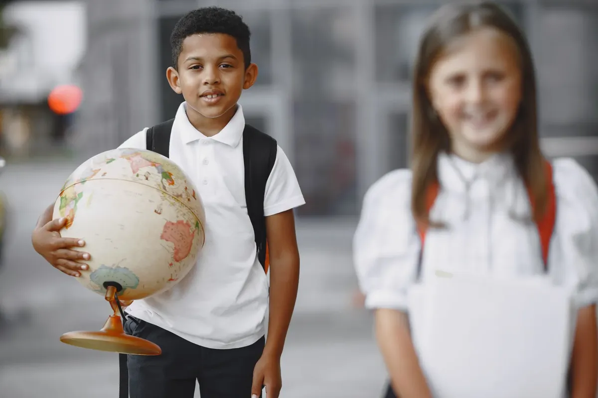 Two smiling students holding a globe and notebooks outside a school.