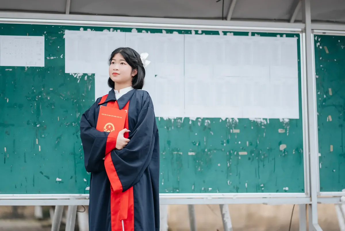 学士号を手にし、外の掲示板の前で立っている毕业生。