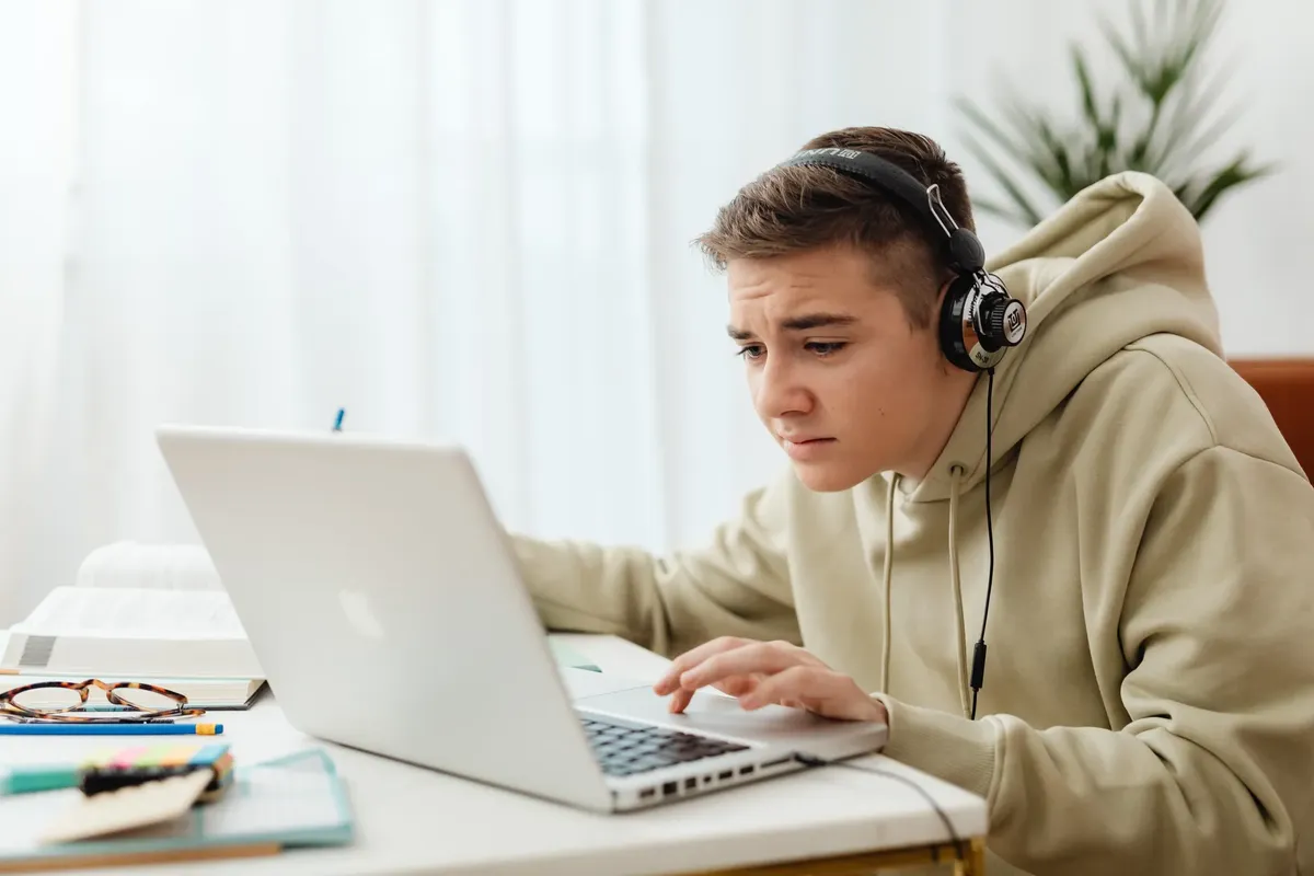 Teen wearing headphones studies online with a laptop in a cozy indoor setting.